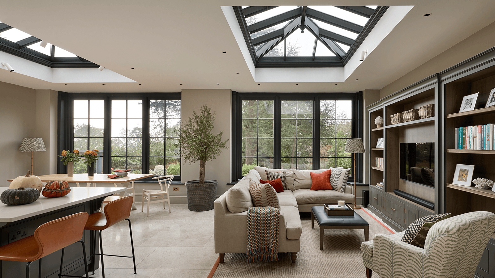 Modern living room with large windows, skylights, orangeries-inspired decor, and pops of orange near a kitchen island.