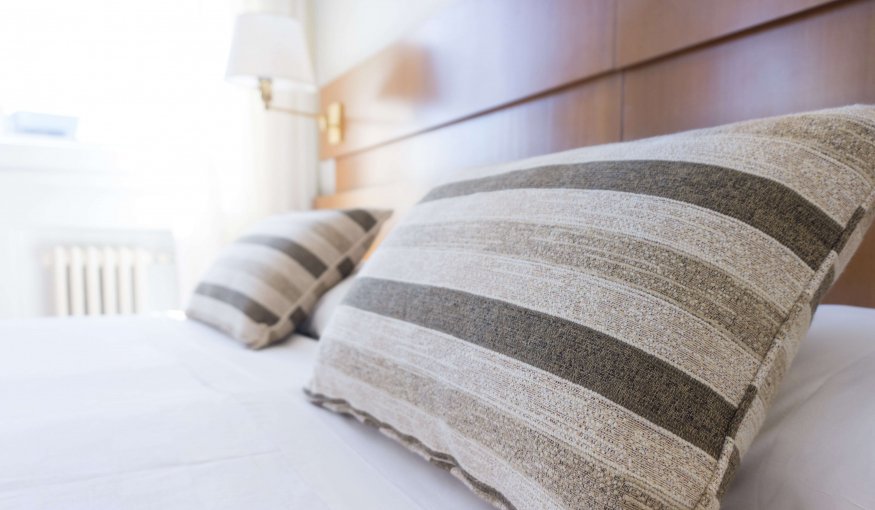 Close-up of two striped pillows on a neatly made bed with white sheets in a bright, modern room.